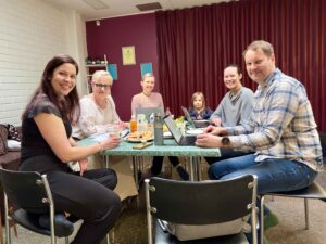 Pöydän ympärillä istumassa hymyileviä naisia, miehiä ja lapsia.