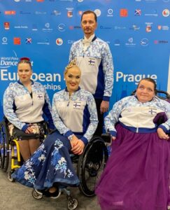 Kuvassa poseeraa kolme paratanssijanaista pyörätuoleissa ja yksi pystytanssija mies.