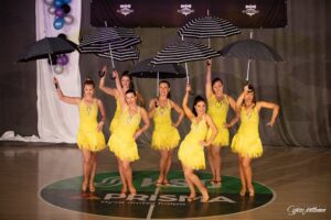 Naisia keltaisissa esiintymisasuissa sateenvarjot käsissä.