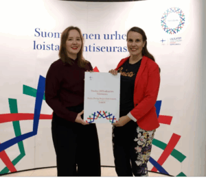 Kaksi naista seisoo katsoen kameraan ja pitävät yhdessä kunniakirjaa.