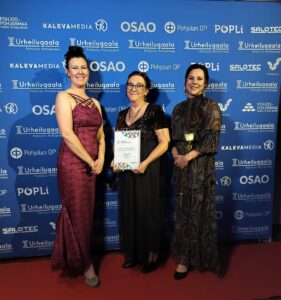 Kolme naista gaala-tilaisuudessa kunniakirja esillä.