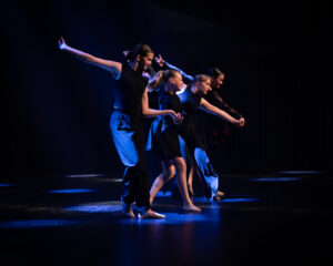 Tyttöjä tanssimassa mustalla lavalla sinisessä valossa.