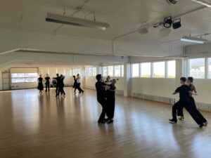 Aikuispareja tanssimassa isossa aurinkoisessa salissa.