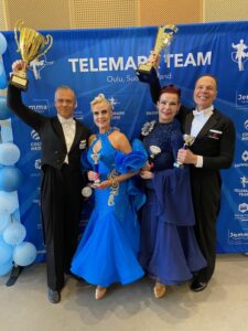 Kaksi senioriparia vakiotanssiasuissa iloitsevta pokaalit kädessä voitoista.