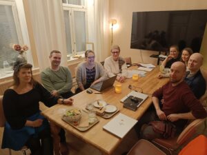 Miehiä ja naisia istuu kokouspöydän ympärillä ja katsoo kameraan.